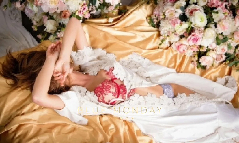 an escort posing on a bed with flowers in lingerie